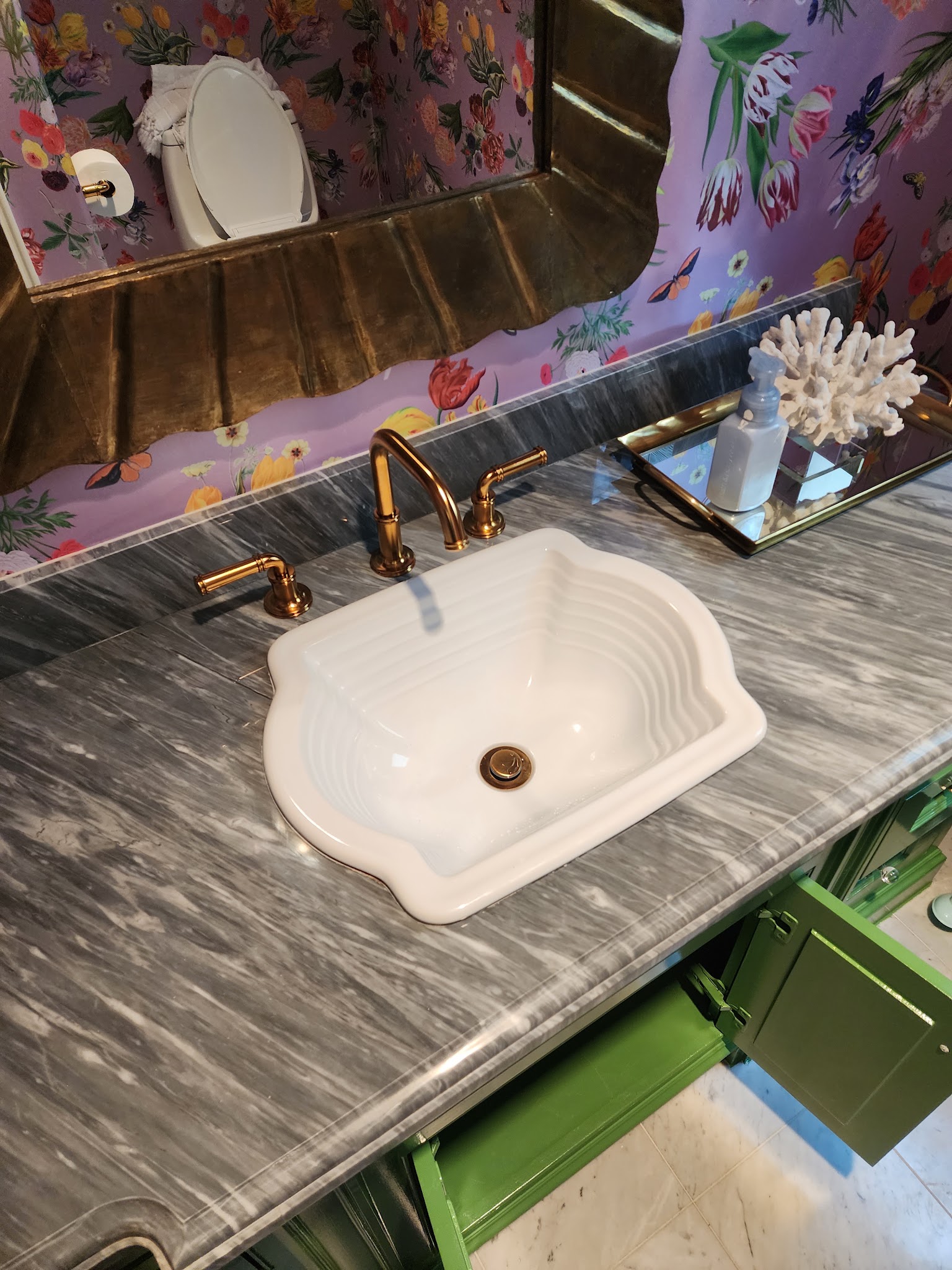 Copper faucet on a green vanity with marble top and floral wallpaper